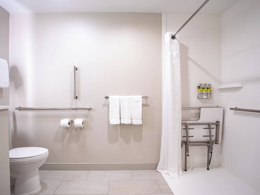 A bathroom with a toilet, a shower with a grab bar, a sink with a mirror, and a towel rack.