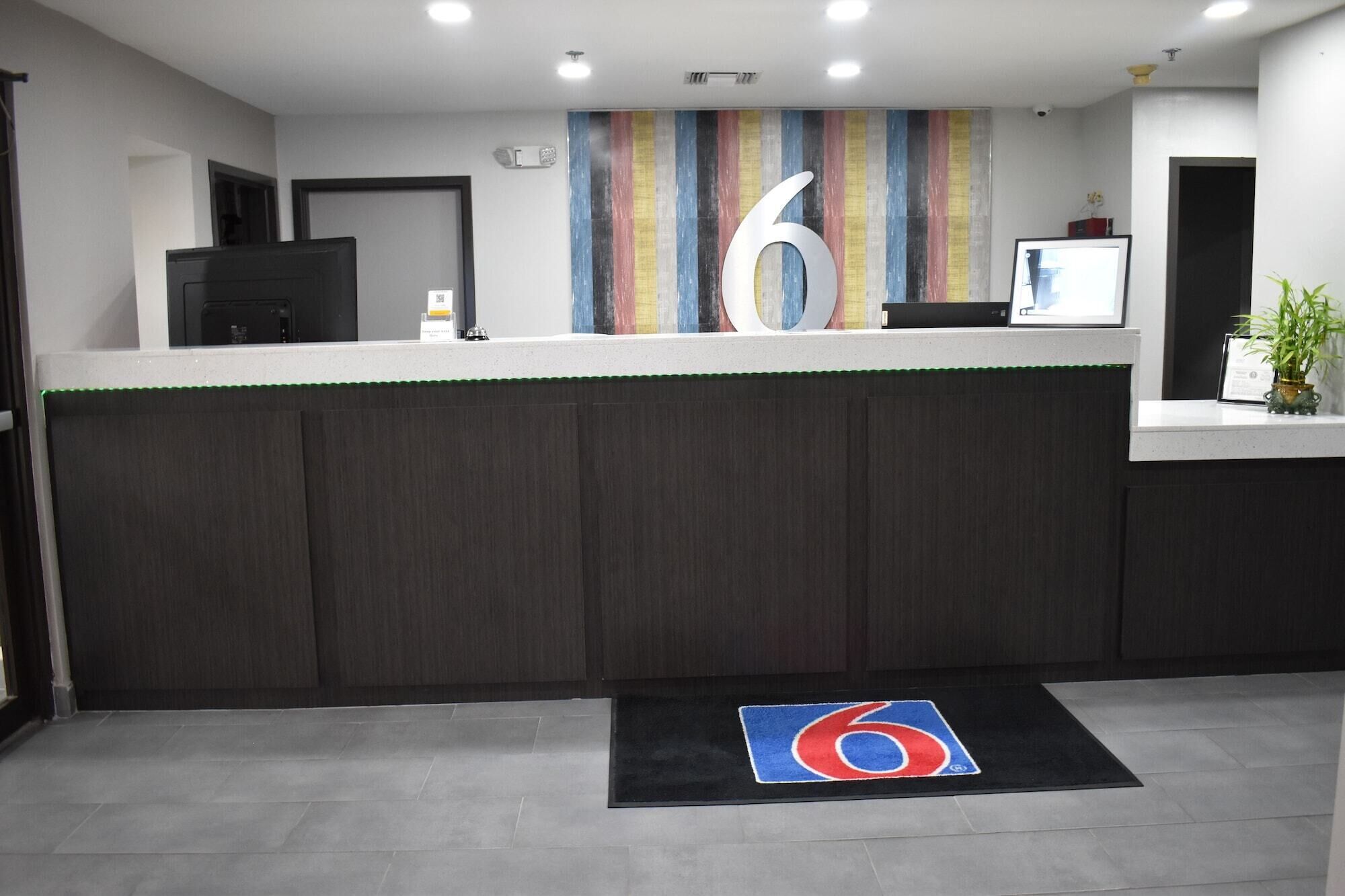 A reception area with a large number '6' on the wall, a reception desk, a plant, and a black mat with the number '6' on it.