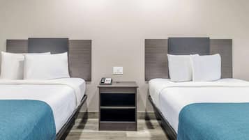 A hotel room with two beds, a nightstand with a phone, and a wall socket.