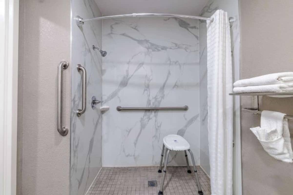 Une salle de bain avec une douche à parois de verre, des murs en marbre, un porte-serviettes blanc et un petit tabouret blanc.
