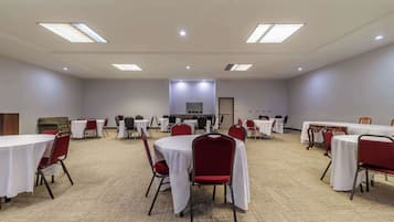 Un salón de conferencias con varias mesas y sillas, piso alfombrado e iluminación en el techo.
