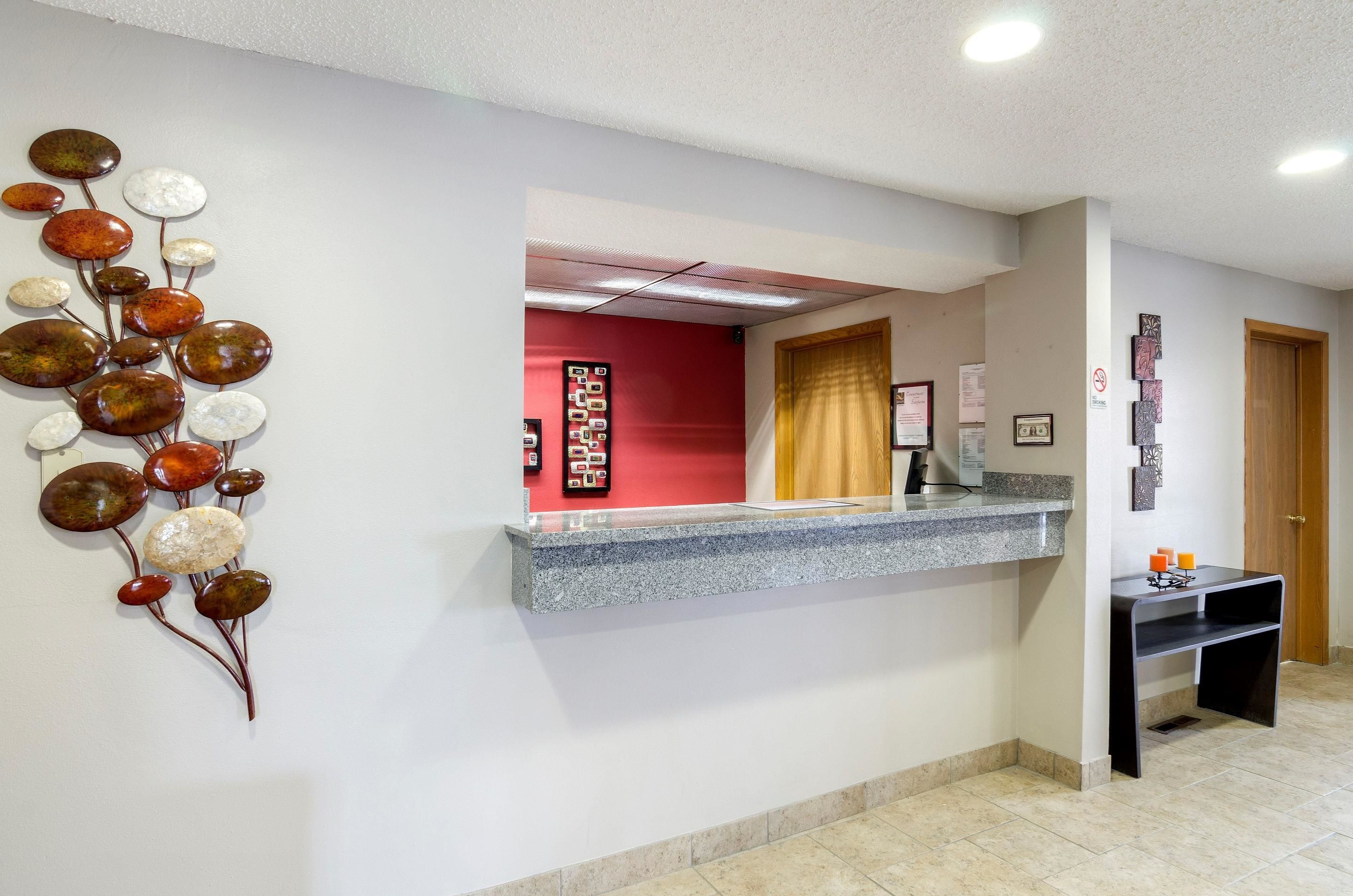 Un espace d’accueil doté d’un comptoir en marbre, d’un mur d’accent rouge et d’un élément décoratif mural.