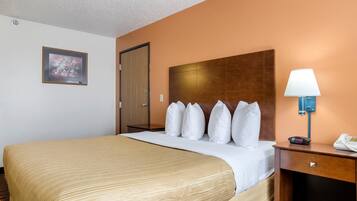 A hotel room with a large bed, a wooden headboard, a bedside table with a lamp, and a framed picture on the wall.