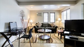 A living room with a sofa, a coffee table, a TV, a laptop, and a desk.