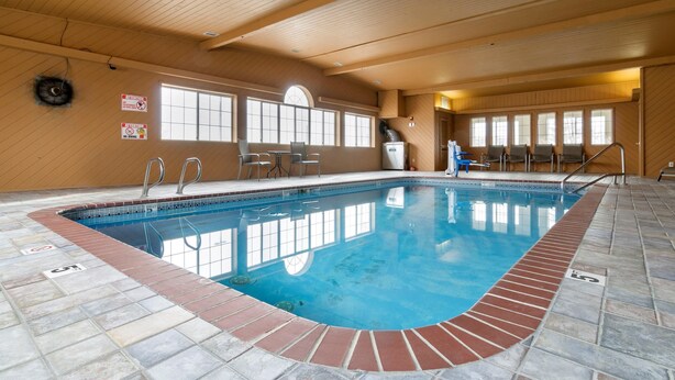 An indoor swimming pool with clear water, tiled floor, and wooden walls.