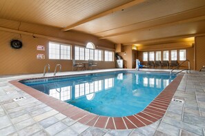 An indoor swimming pool with clear water, tiled floor, and wooden walls.
