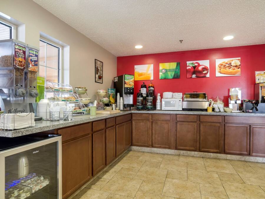 A kitchen with a red wall, various appliances, and a beverage dispenser.