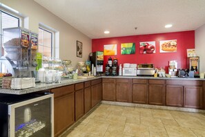 A kitchen with a red wall, various appliances, and a beverage dispenser.