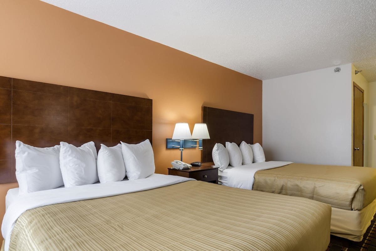 A hotel room with two beds, a nightstand with a lamp, and a telephone.