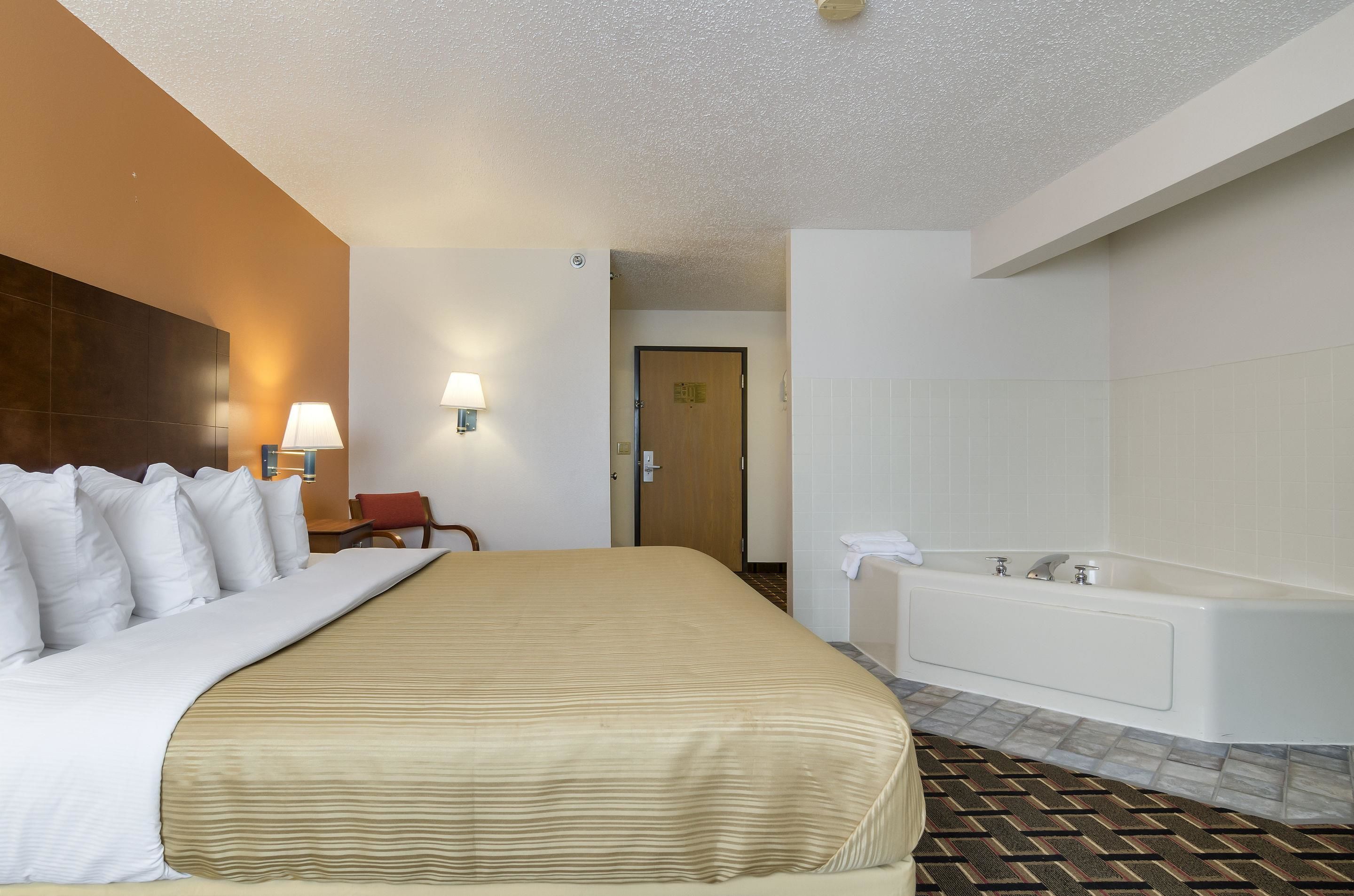 Una habitación de hotel con una cama grande, un baño con bañera y una puerta que da a otra habitación.