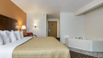 Una habitación de hotel con una cama grande, un baño con bañera y una puerta que da a otra habitación.
