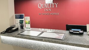 A reception desk at Quality Inn by Choice Hotels with a red wall, a phone, a digital kiosk, and informational brochures.