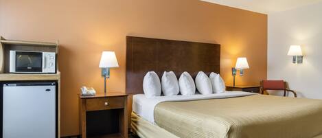 Habitación de hotel con cama, microondas, refrigerador, escritorio y dos lámparas.