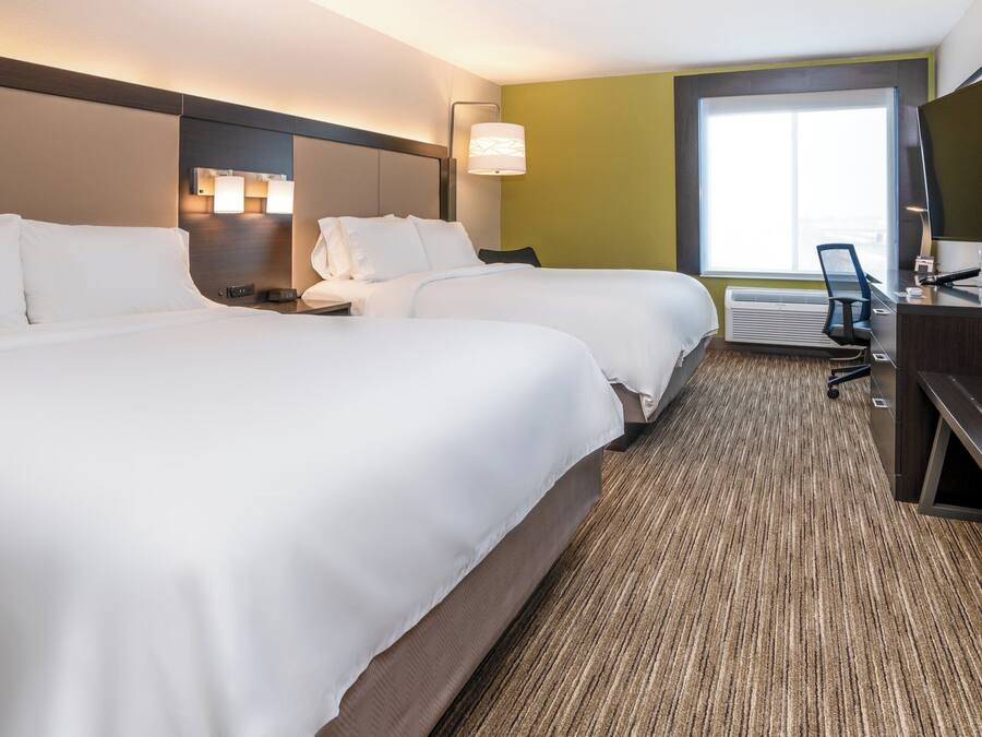 A hotel room with two beds, a desk, a TV, and a large window.