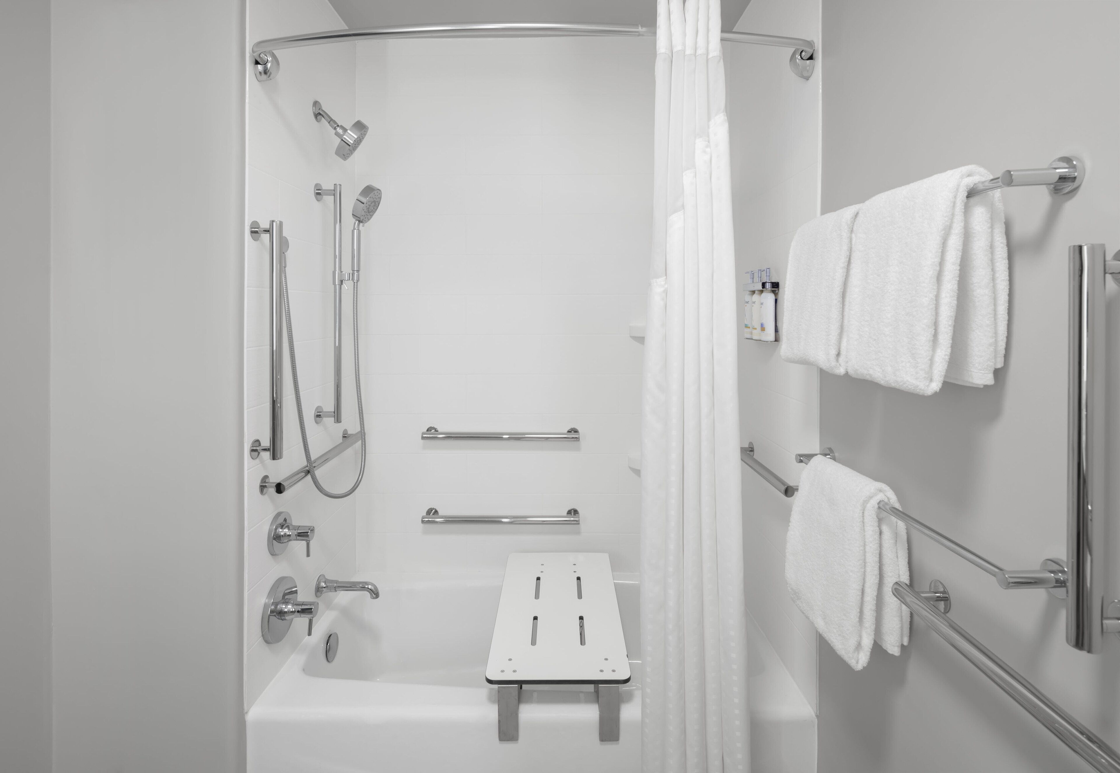 A modern bathroom with a walk-in shower, grab bars, a bench, and towel racks.