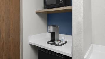 Eine Küchenzeile mit Mikrowelle, Kaffeemaschine und kleinem Kühlschrank.