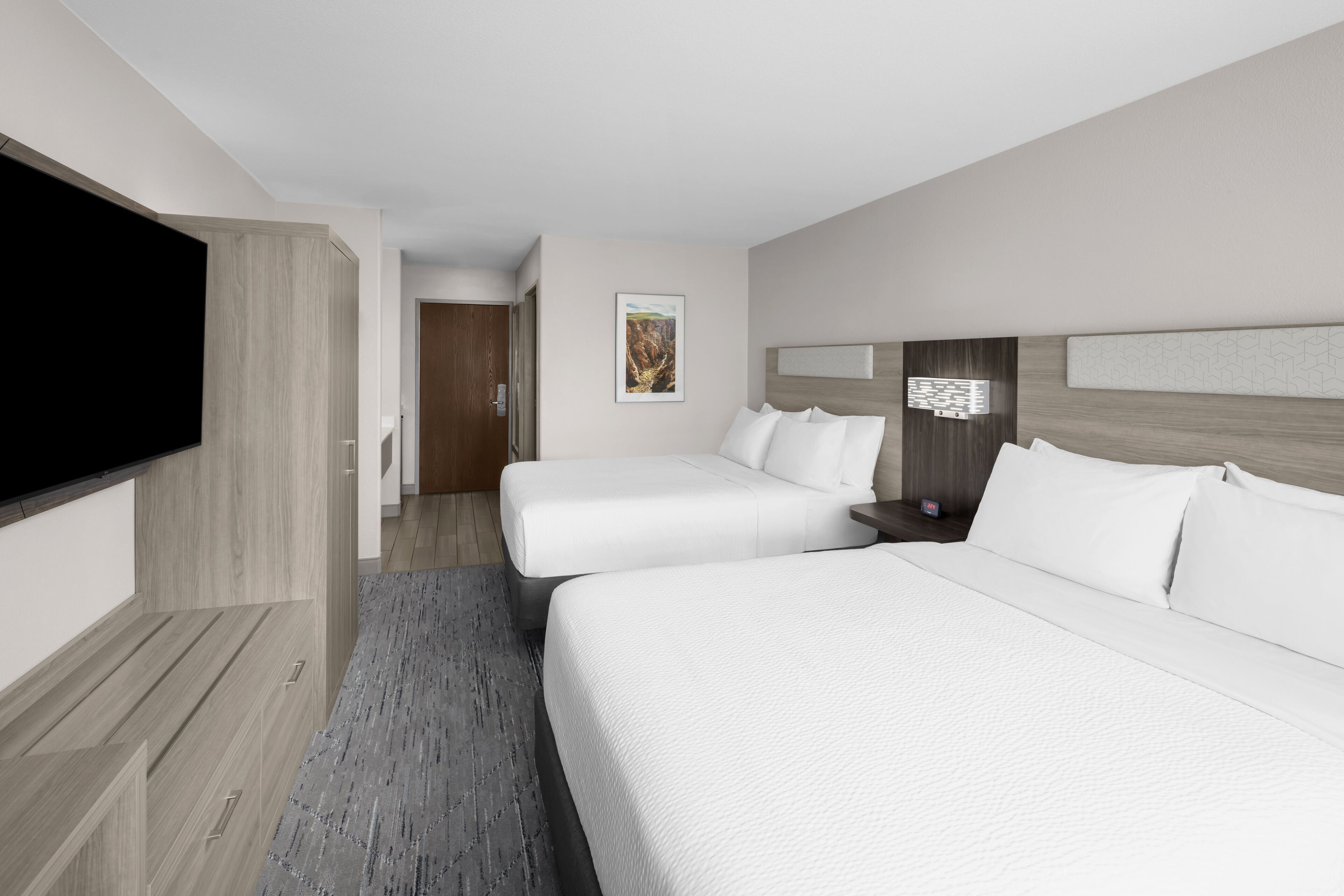 Habitación de hotel con dos camas, un televisor de pantalla plana, un armario de madera y un cuadro en la pared.