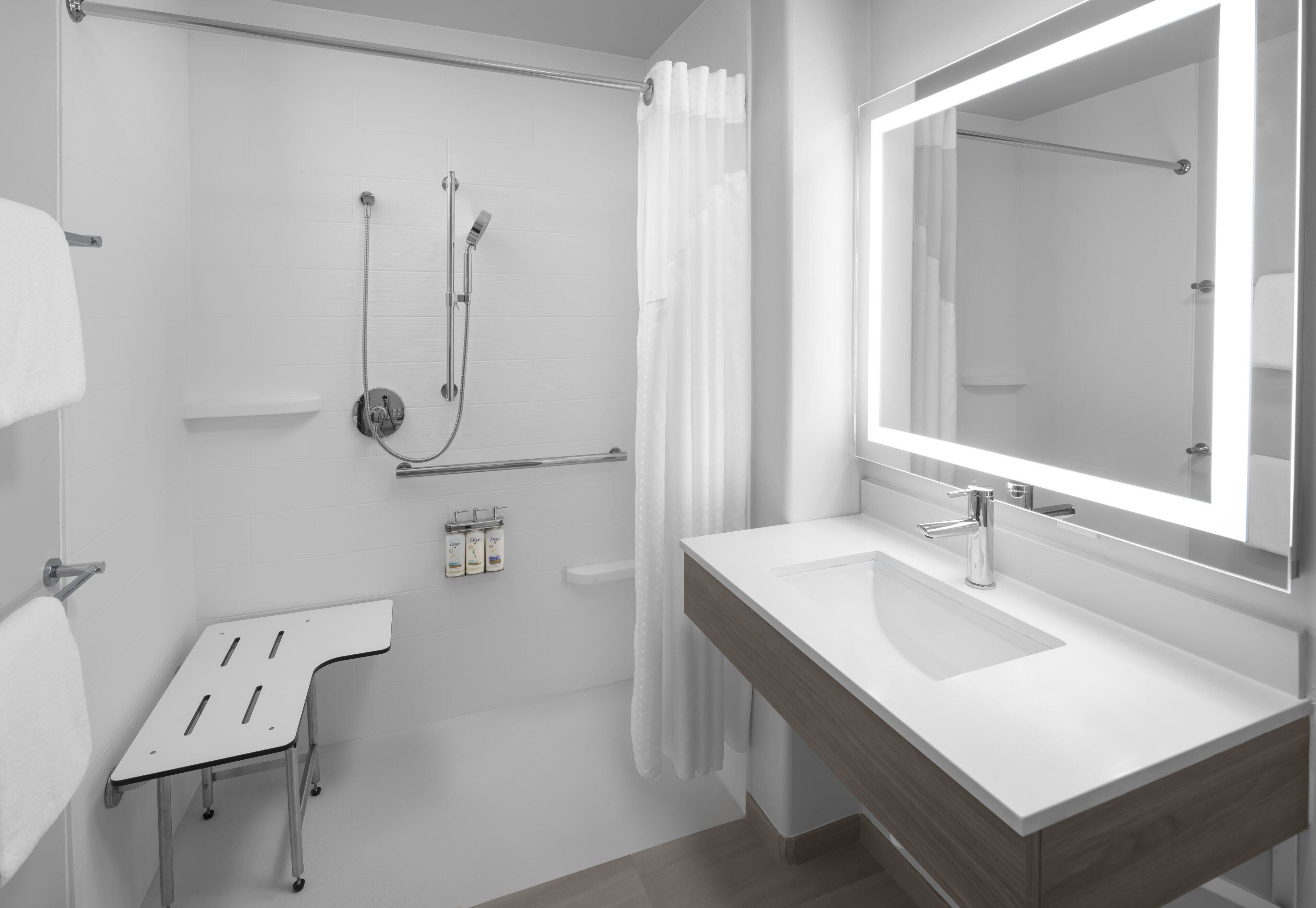 Un bany modern amb un lavabo blanc, un mirall gran, una dutxa amb porta de vidre i una tovallola blanca penjada a la paret.