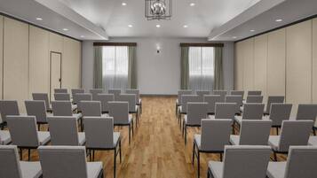 Konferenssihuone, jossa on riveissä harmaita tuoleja, puulattia ja suuri kattokruunu.