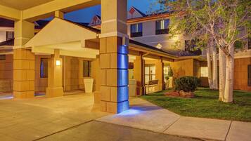 A hotel entrance with a covered walkway, a well-maintained lawn, and a tree.