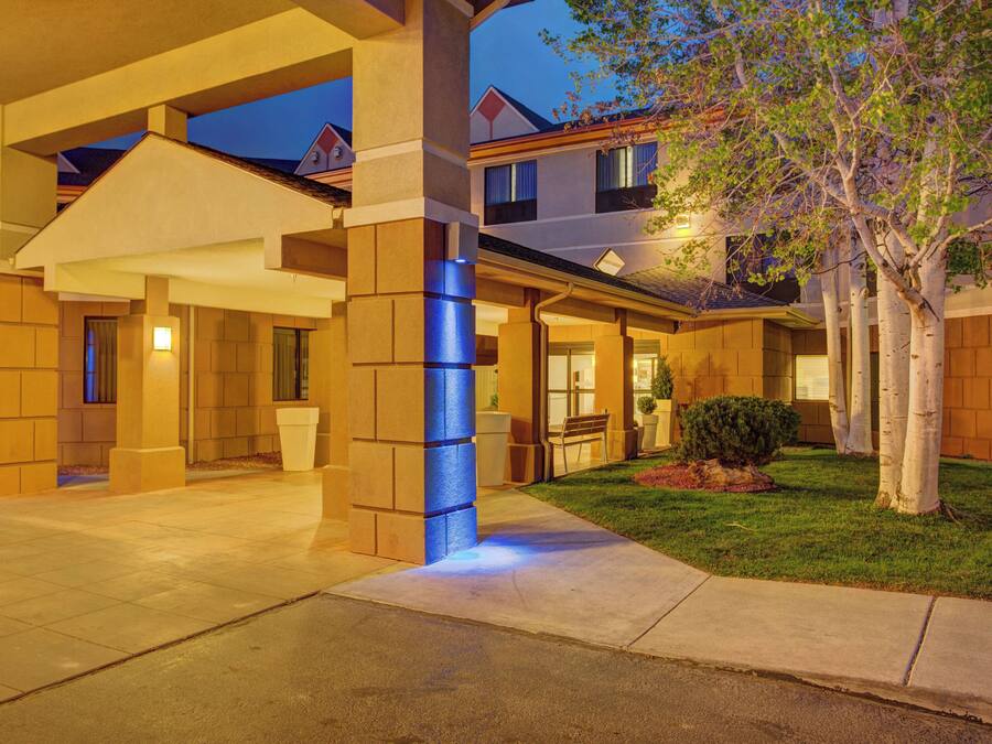 A hotel entrance with a covered walkway, a well-maintained lawn, and a tree.