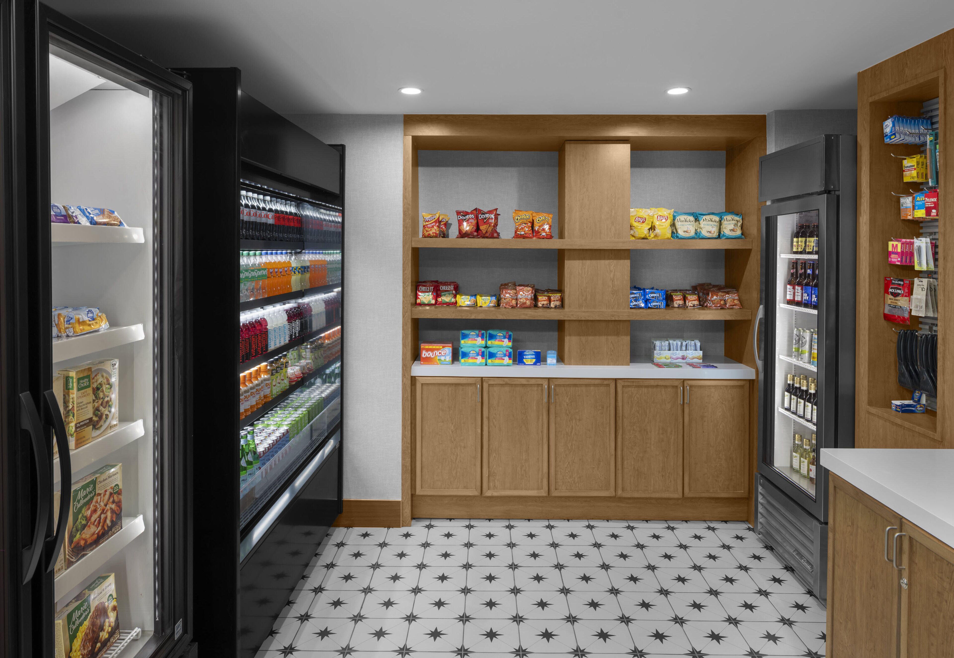 Une cuisine compacte équipée d’un réfrigérateur, de quelques étagères remplies d’en-cas et d’un sol carrelé.