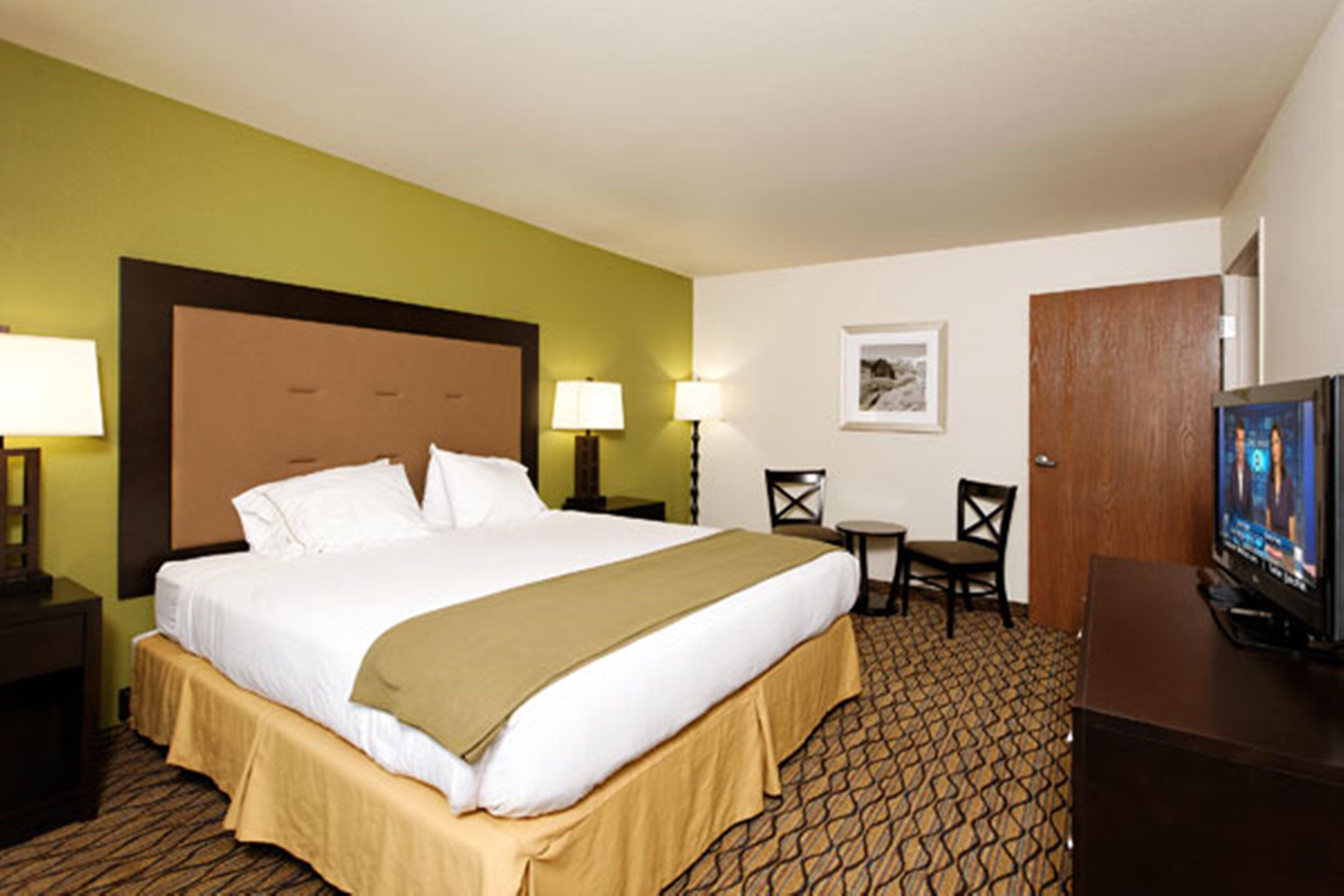 A hotel room with a large bed, two bedside lamps, a television, a small table with two chairs, and a framed picture on the wall.