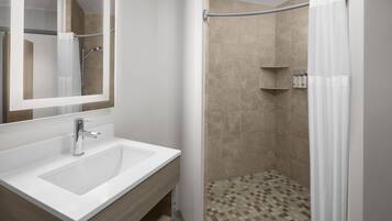 Een moderne badkamer met een grote spiegel, een wit wastafelmeubel en een douchehoek.