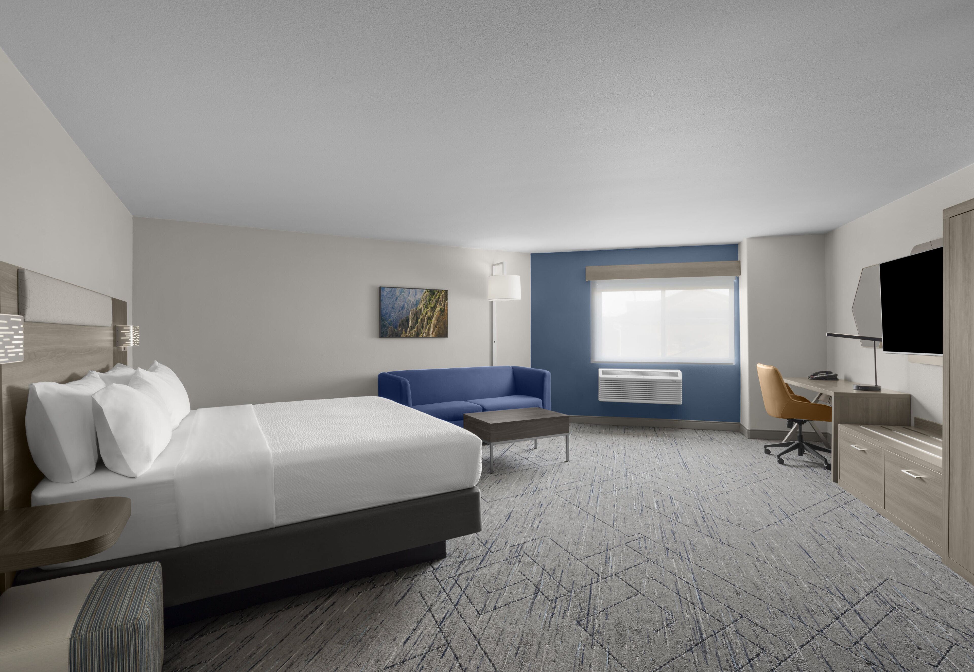A modern hotel room with a large bed, a blue sofa, a desk, and a TV.