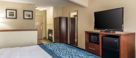 A hotel room with a bed, a television, a refrigerator, and a wardrobe.