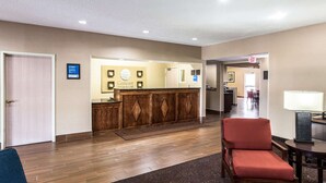 A hotel reception area with a wooden reception desk, a red chair, and a carpeted floor. - Comfort Inn & Suites - Hannibal (Hannibal)