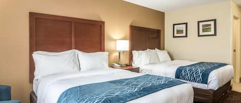 A hotel room with two beds, a nightstand with a lamp, and two framed pictures on the wall.