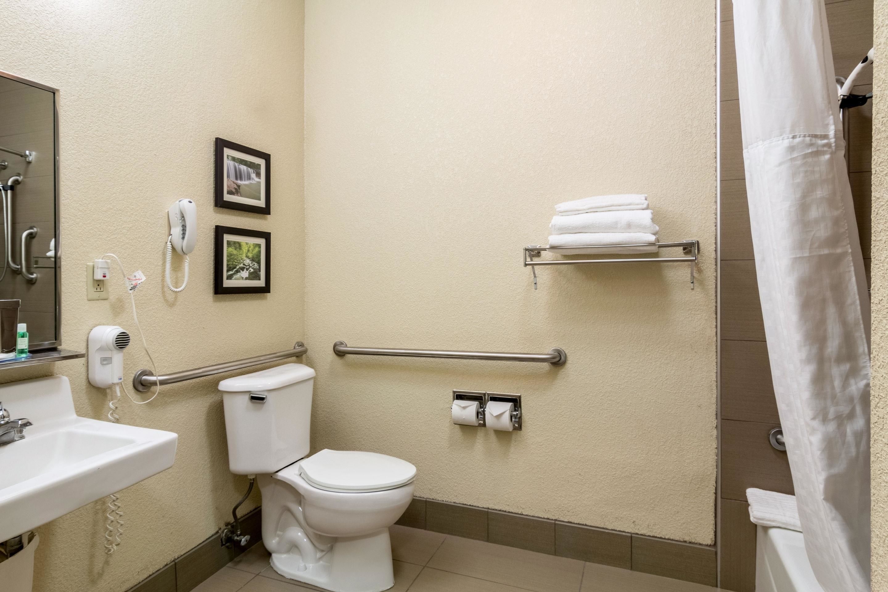 Een badkamer met toilet, wastafel en douche. Er zijn handdrogers, een telefoon en een handdoekrek.