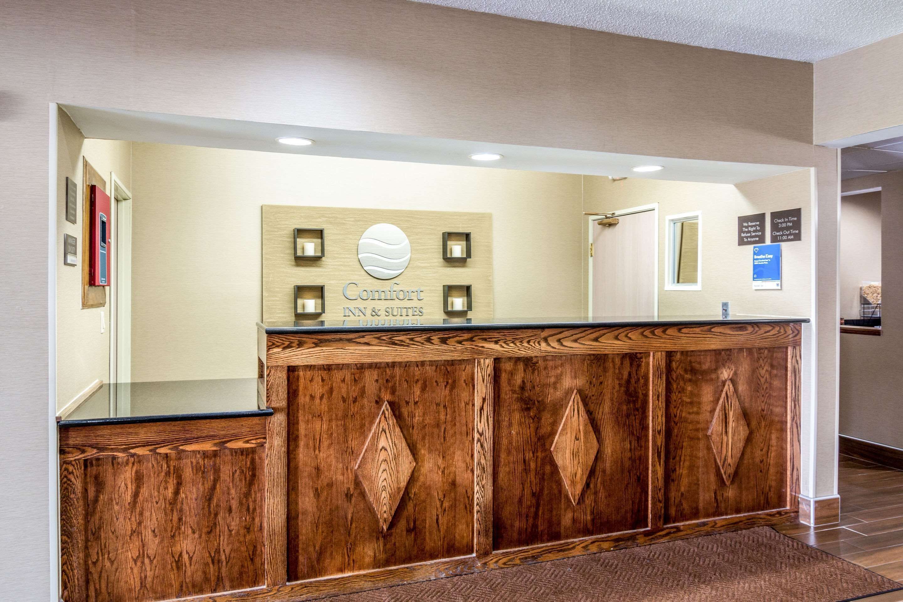 Un mostrador de recepción con detalles de madera, un cartel que dice "Comfort Inn & Suites" y una zona de registro.