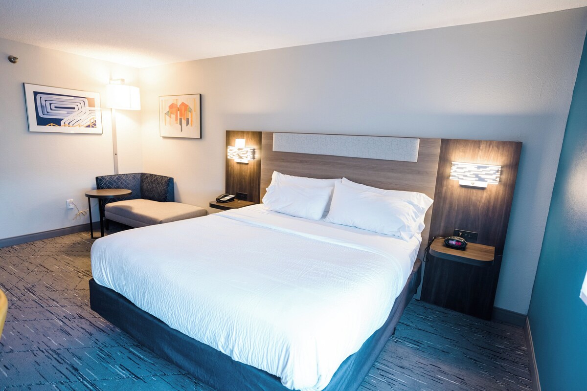 A hotel room with a large bed, a desk, a chair, and two wall-mounted lamps.