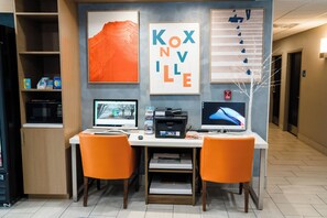 A reception desk with two computer monitors, a printer, and orange chairs.