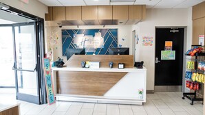 Zona de recepción con mostrador de madera, un letrero que dice "Hollyday Inn Express" y una máquina expendedora de aperitivos.