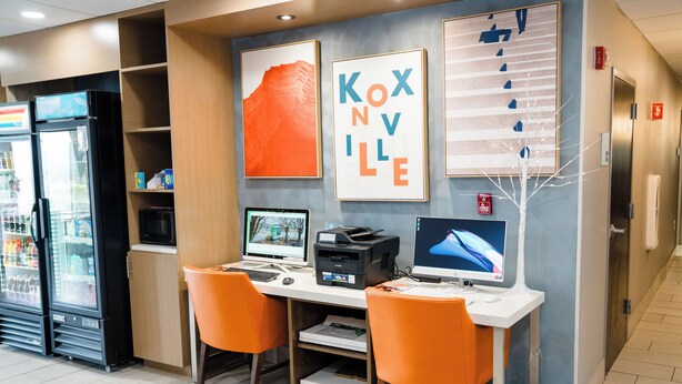 Un vestíbulo de hotel con una recepción, dos computadoras, un refrigerador y un extintor.