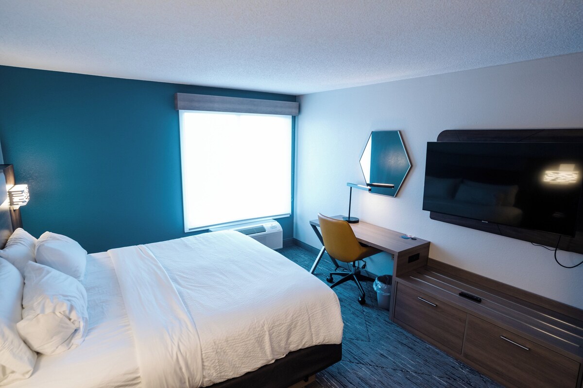A hotel room with a bed, a desk, a chair, a television, and a window.