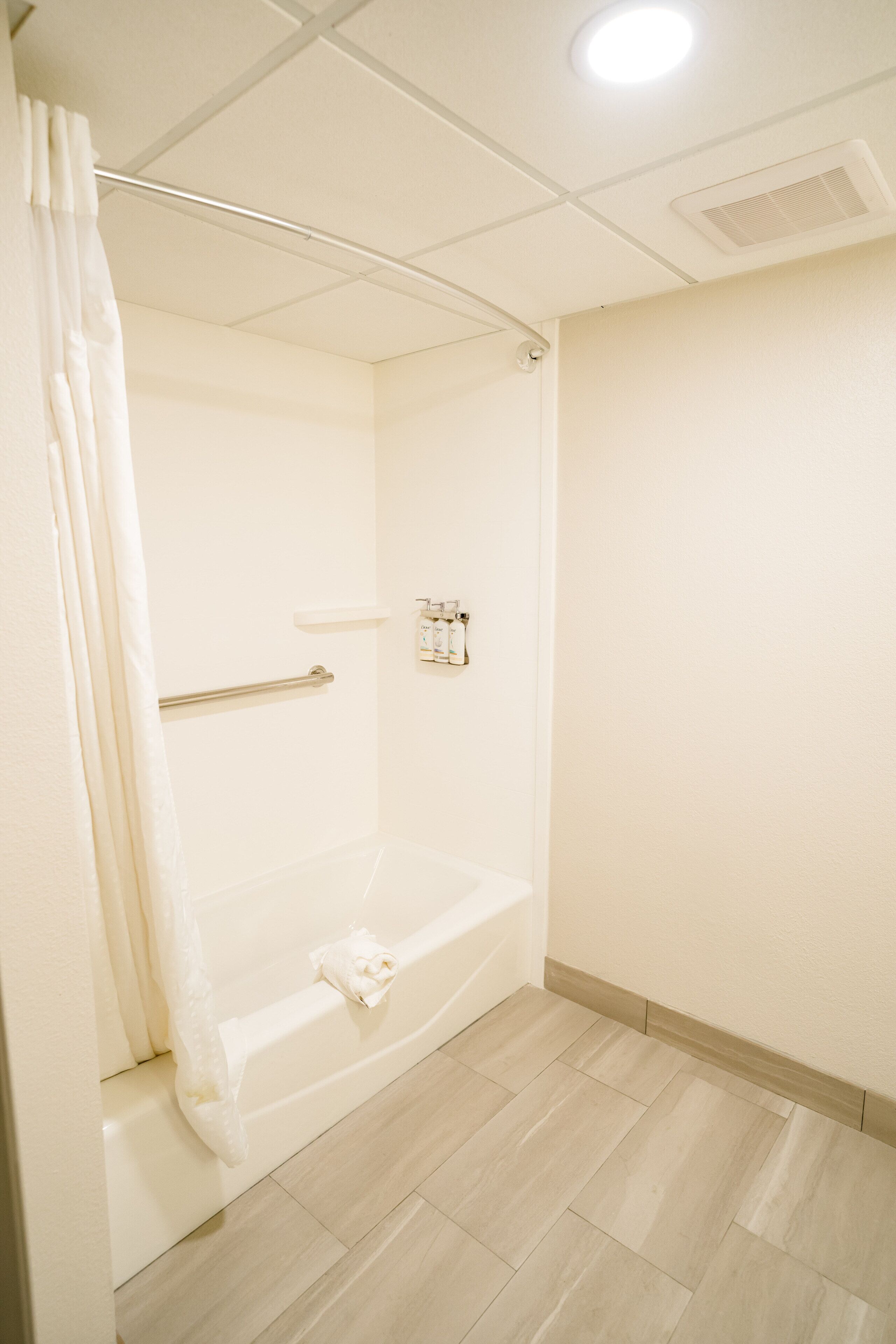 A bathroom with a bathtub, a shower curtain, a towel rack, and a wall-mounted light fixture.