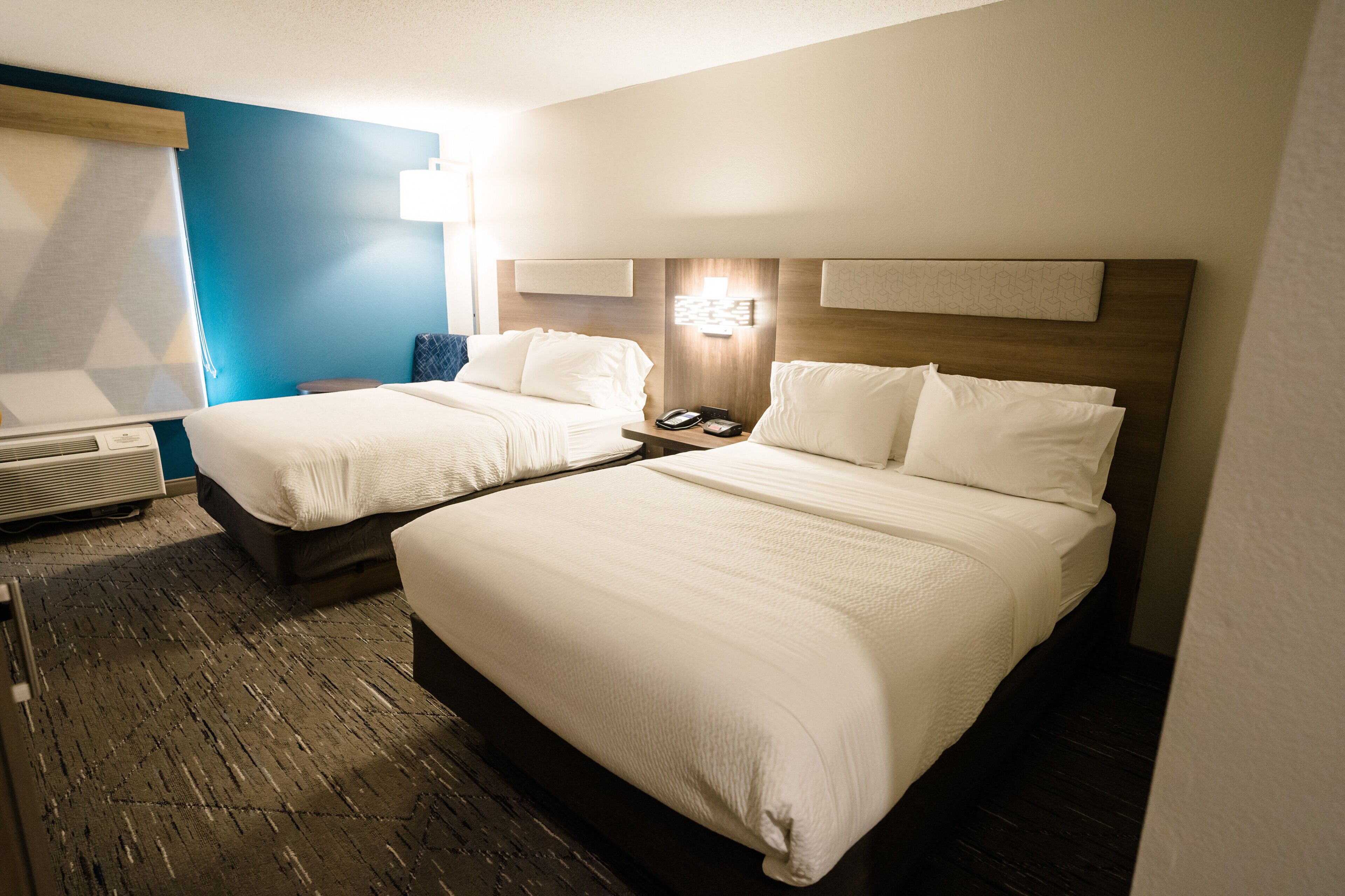 A hotel room with two beds, a desk, a chair, and a window with blinds.