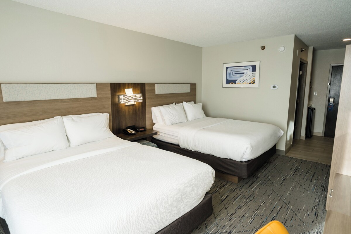 A hotel room with two beds, a nightstand, a wall-mounted light, and a framed picture.