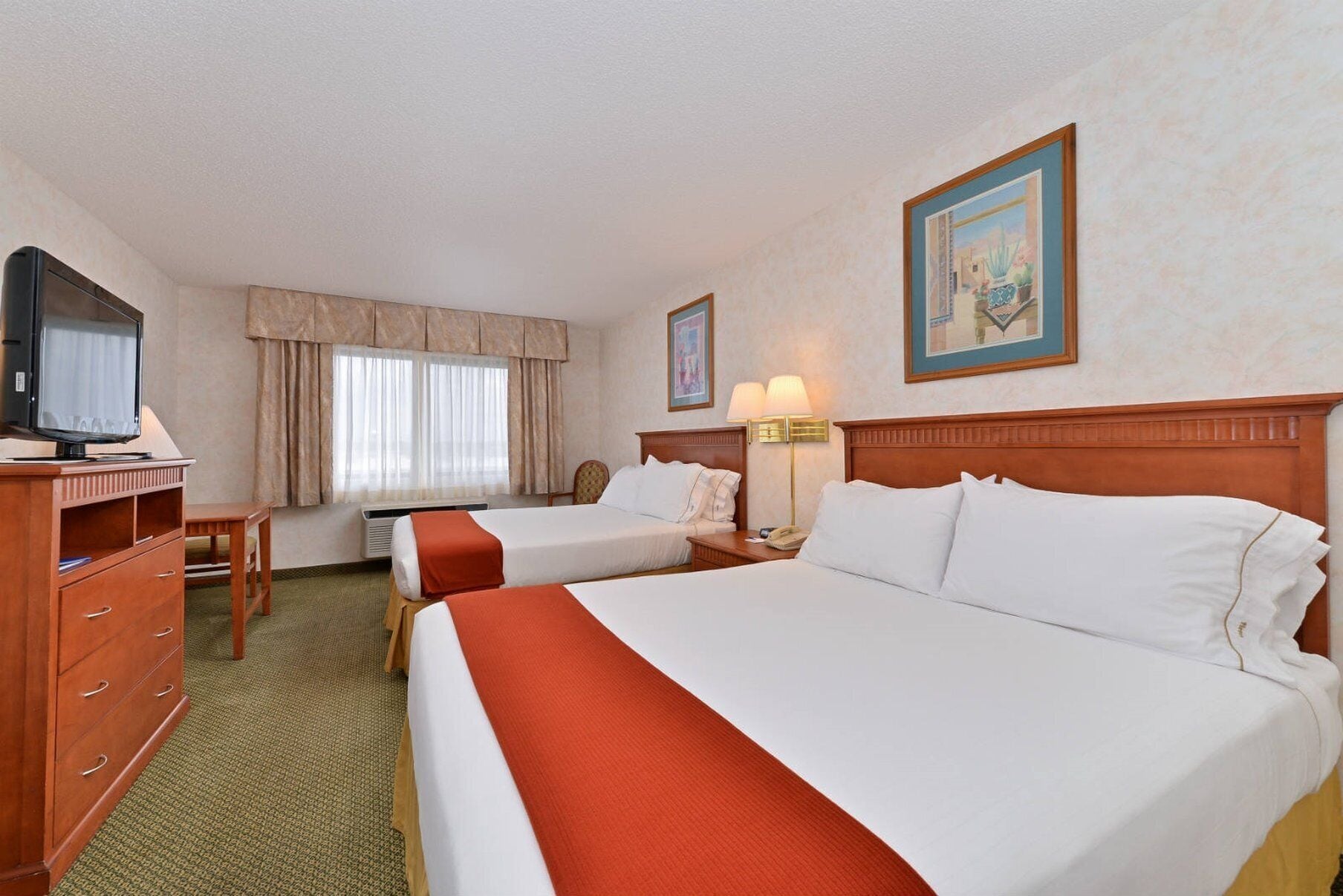 A hotel room with two beds, a desk with a television, a lamp, and a framed picture on the wall.