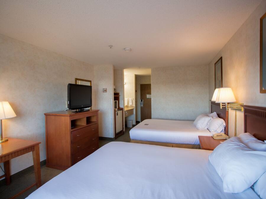 A hotel room with two beds, a desk with a television, and lamps.