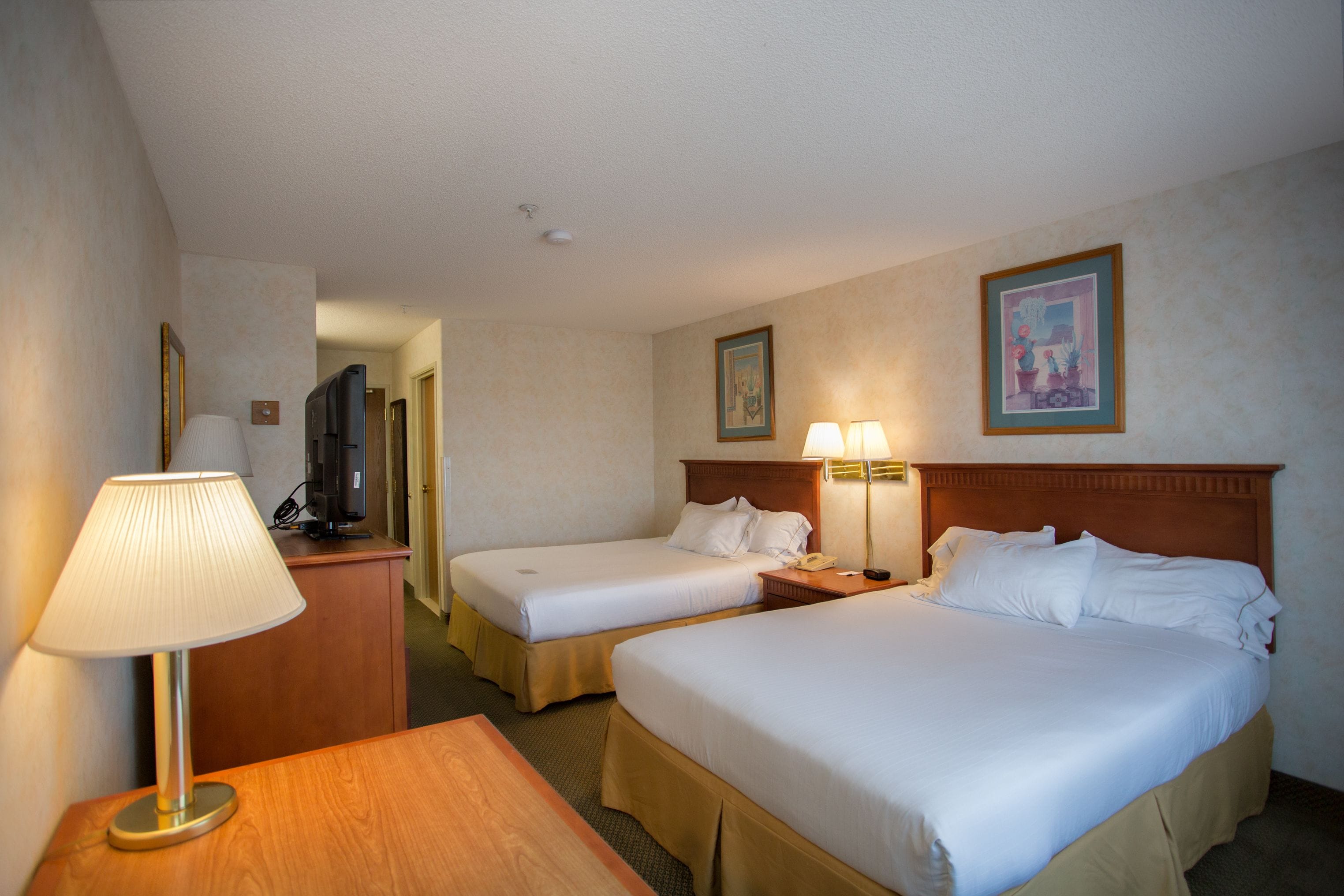 A hotel room with two single beds, a desk with a lamp, a TV, and a painting on the wall.