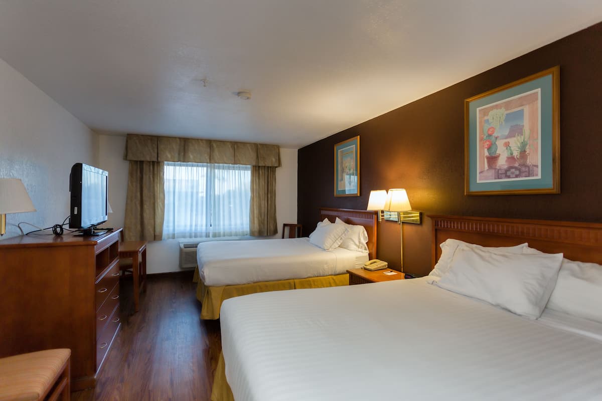 A hotel room with two beds, a desk with a television, and a window with curtains.