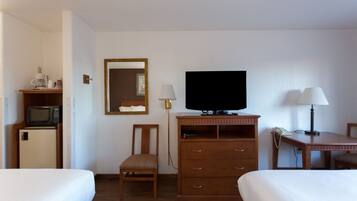 Habitación de hotel con dos camas, televisión, escritorio con lámpara, silla, cómoda de madera y microondas.