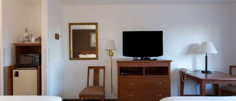 A hotel room with two beds, a television, a desk with a lamp, a chair, a wooden dresser, and a microwave.