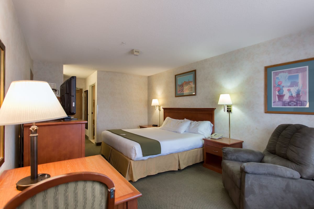 A hotel room with a bed, bedside table, lamp, chair, and a television on a cabinet.