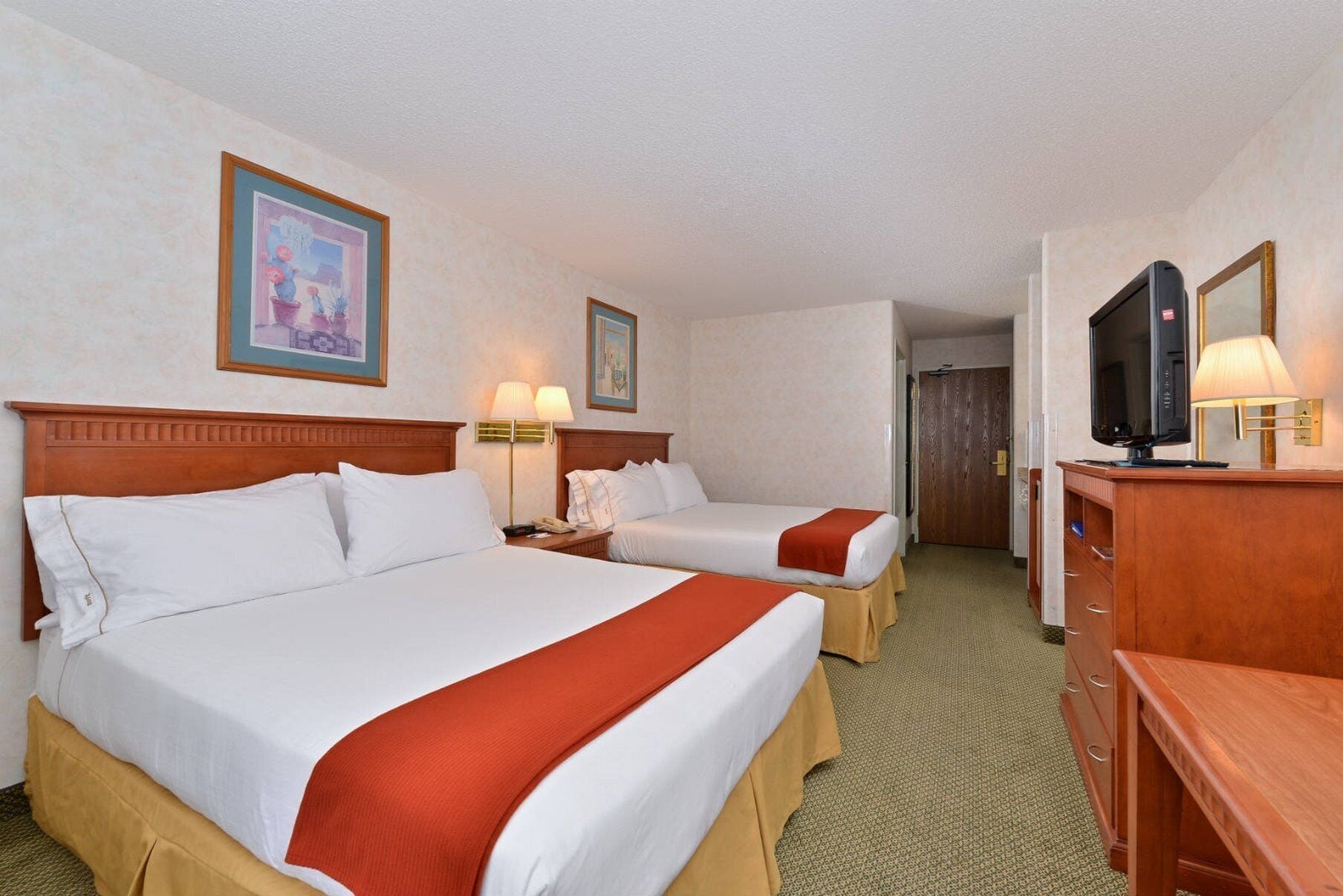 Una habitación de hotel con dos camas, televisión, escritorio y lámpara.